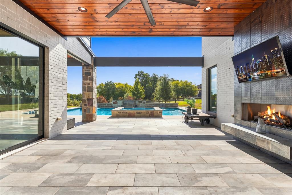 Covered outdoor patio featuring a wood-plank ceiling, floor-to-ceiling stone-surround fireplace, tile flooring, and integrated recessed lighting, opening to a swimming pool and spa