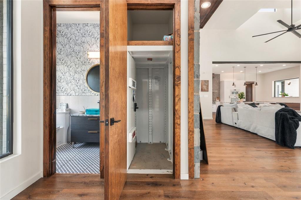 Interior residential elevator featuring an industrial-style metal cab, wood-finish flooring, and natural wood door casing