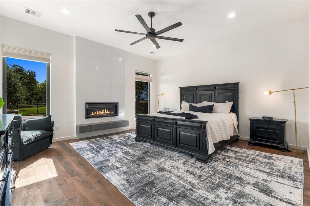 Spacious room featuring wood-finish flooring, a linear fireplace with a floor-to-ceiling tile surround, a cantilevered hearth, and a modern six-blade ceiling fan