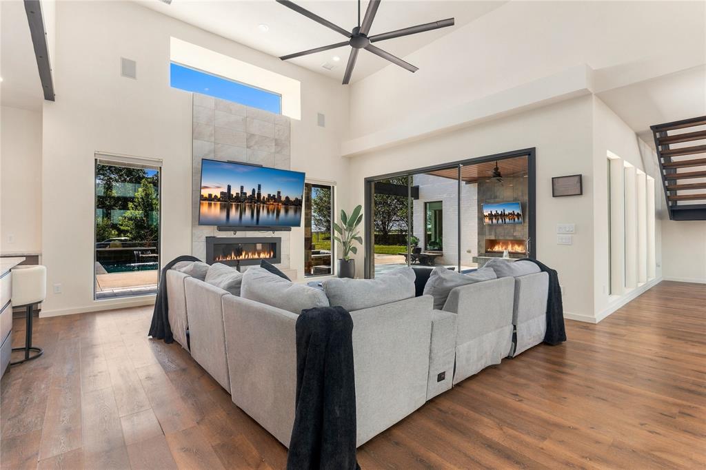 Vaulted ceiling featuring a central multi-blade fan, stone-surround fireplace, large-format glass sliding doors, and wood-finish flooring Vaulted ceiling featuring a central multi-blade fan, stone-surround fireplace, large-format glass sliding doors, and wood-finish flooring