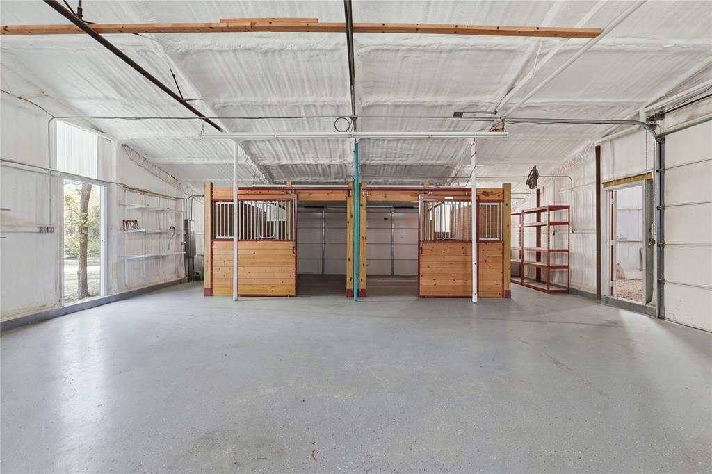 Spacious multipurpose outbuilding featuring concrete flooring, spray-foam insulation, and three wooden horse stalls with metal grating