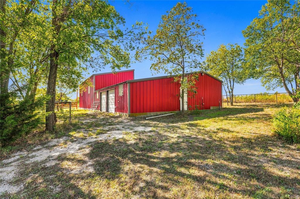 Metal-sided red structure featuring dual garage doors, concrete foundation, and mature trees on a partially cleared lot