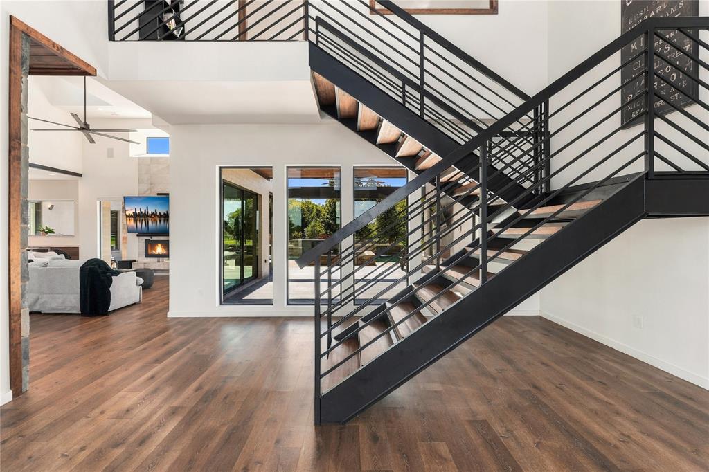 Open-concept interior featuring wood-finish flooring, a floating staircase with black metal railings, triple-pane windows, and high ceilings Open-concept interior featuring wood-finish flooring, a floating staircase with black metal railings, triple-pane windows, and high ceilings