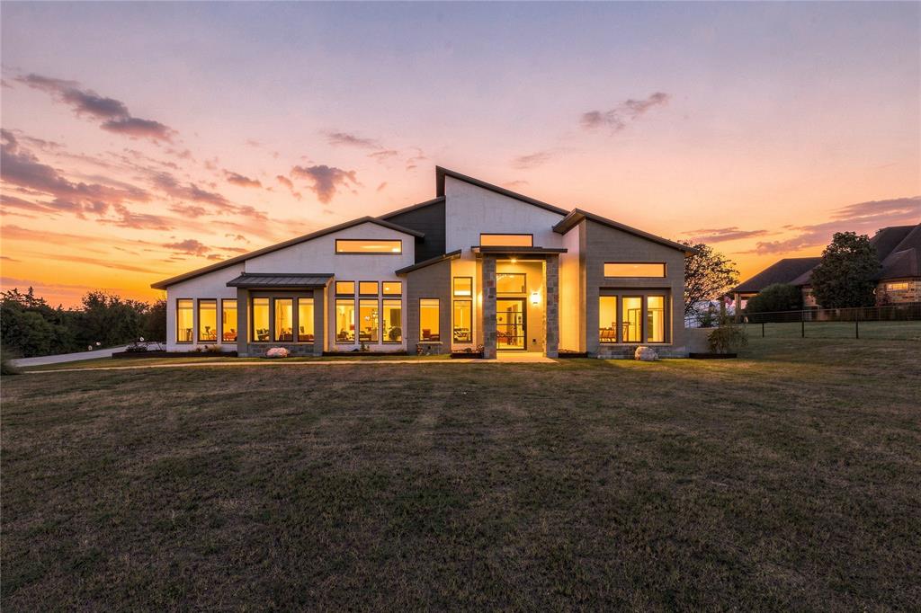 Modern architectural exterior featuring a multi-pitched roofline, stone veneer accents, stucco siding, and extensive floor-to-ceiling windows