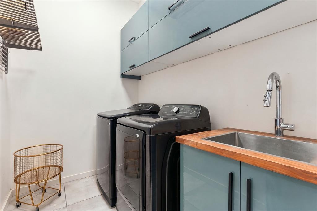 Laundry room featuring slate blue cabinetry with matte black hardware, a wood-finish countertop, a stainless steel undermount sink, and a high-arch pull-down faucet