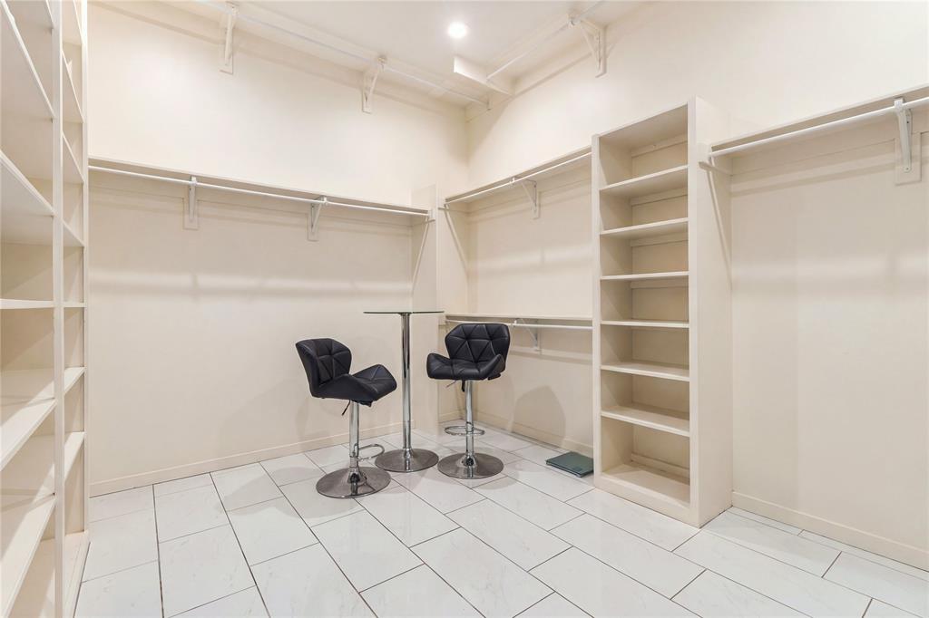 Walk-in storage space featuring custom built-in floor-to-ceiling shelving, multiple tiered hanging rods, and neutral large-format tile flooring