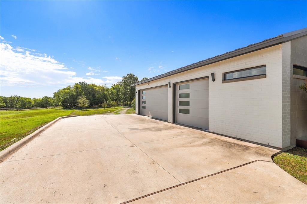 Detached structure featuring a white painted brick exterior, two garage bays with horizontal glass-panel accents, and a concrete apron