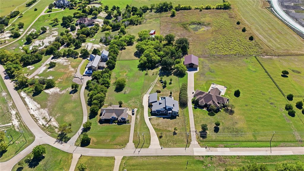 Aerial perspective of expansive acreage featuring multiple residential structures, concrete driveways, and detached outbuildings situated among mature trees and open green space