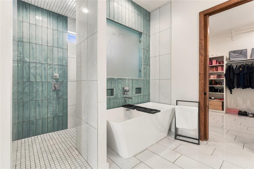 Freestanding soaking tub, large-format vertical blue tile shower surround, mosaic tile shower flooring, and white polished tile flooring