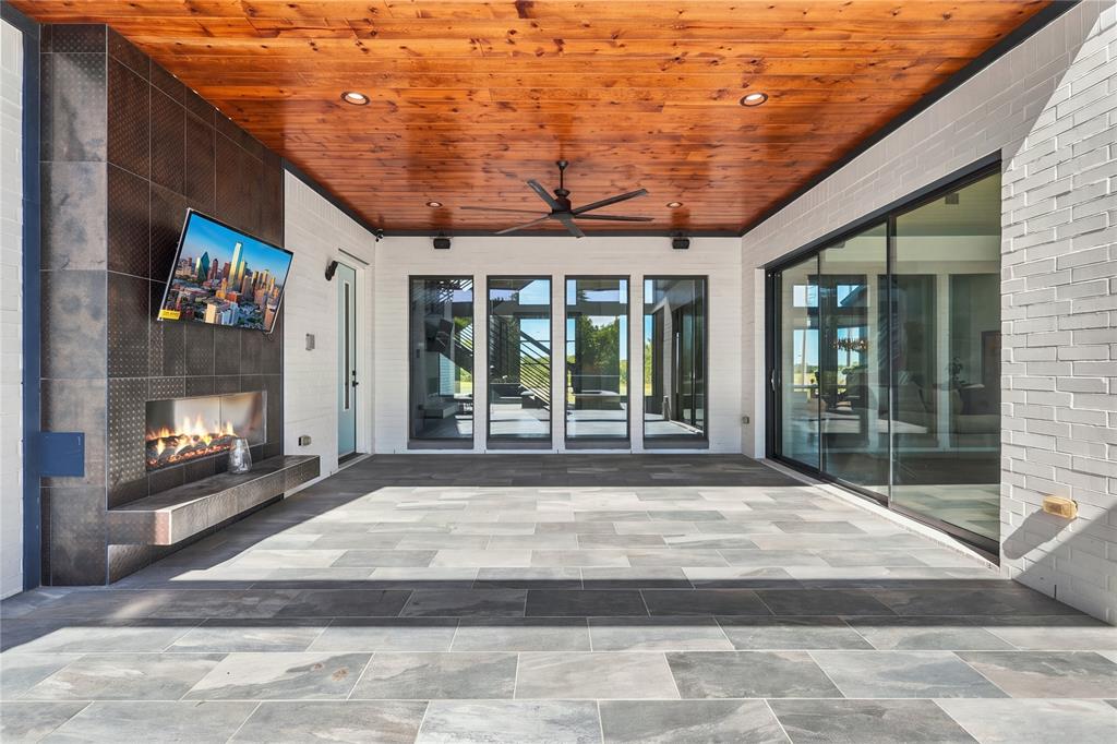 Covered patio featuring a natural wood-finish plank ceiling, large-format tile flooring, a floor-to-ceiling tiled fireplace surround, and expansive sliding glass doors