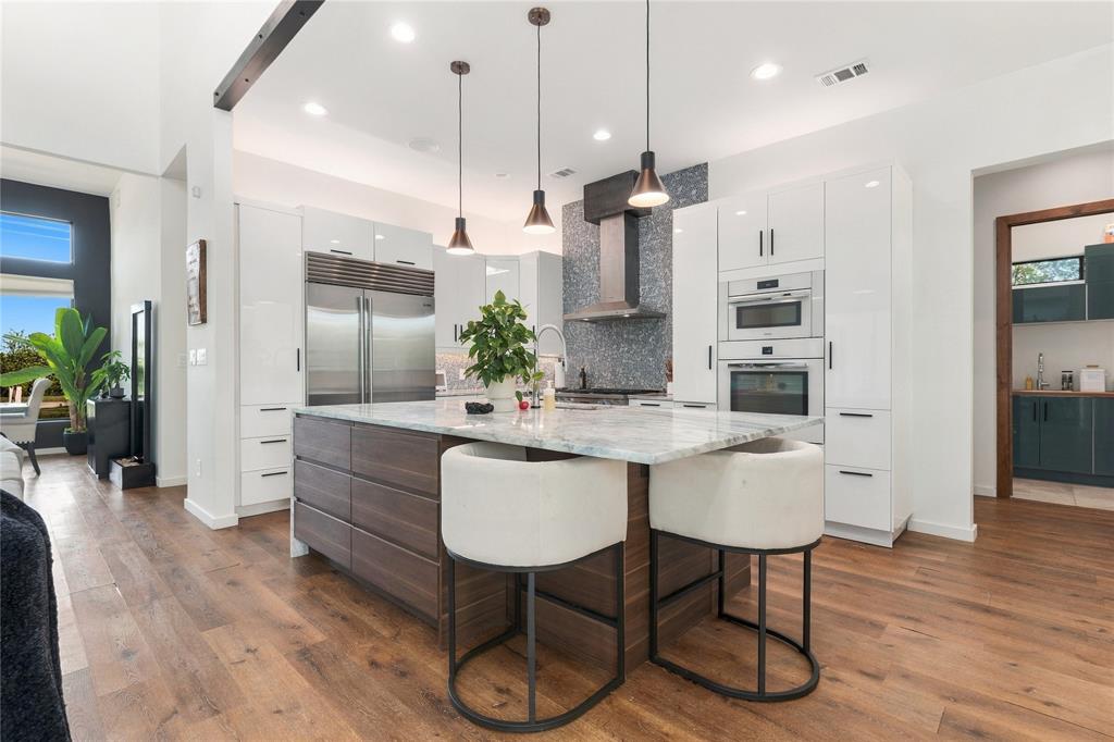 Kitchen featuring high-gloss white cabinetry, wood-finish center island with stone countertop, stainless steel appliances, textured tile backsplash, and recessed lighting Kitchen featuring high-gloss white cabinetry, wood-finish center island with stone countertop, stainless steel appliances, textured tile backsplash, and recessed lighting