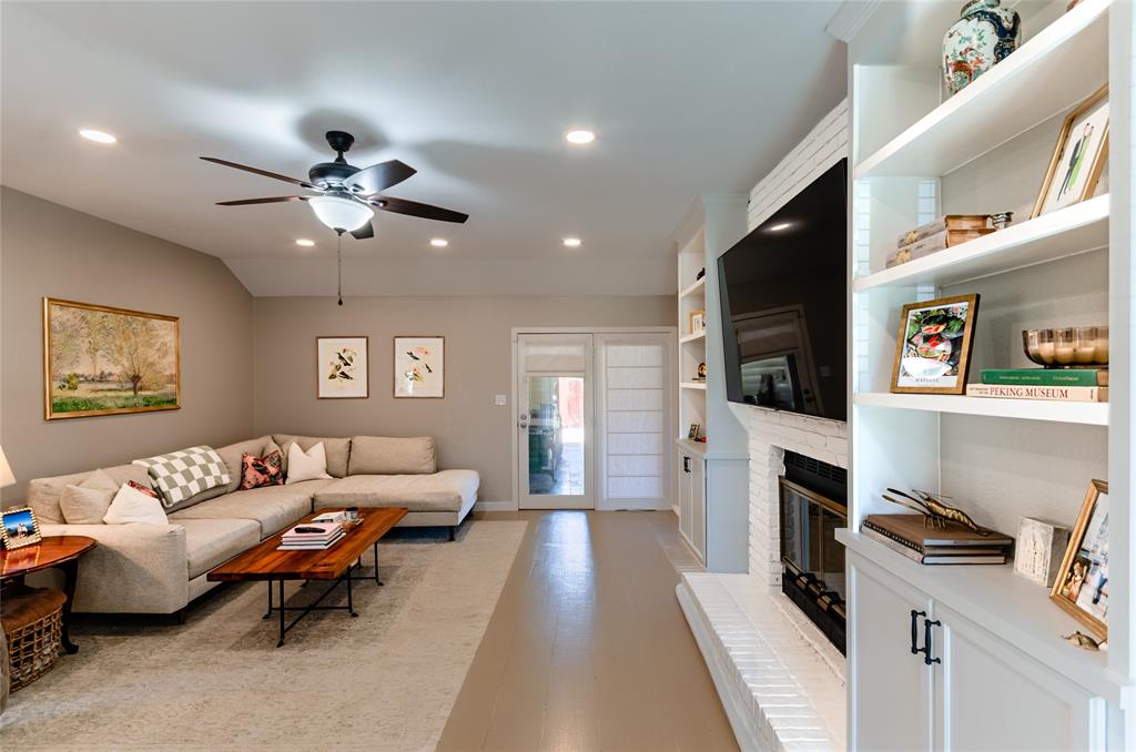 Vaulted ceiling with recessed lighting and ceiling fan, built-in shelving, white brick fireplace, and double glass-paneled doors