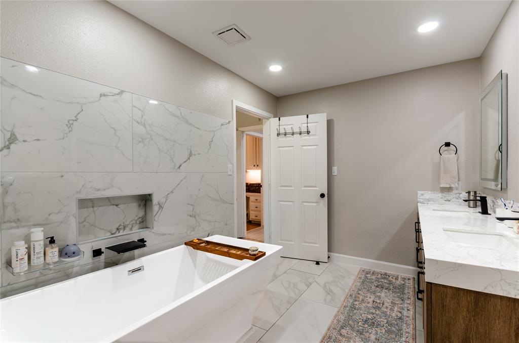 Freestanding soaking tub with a built-in wall niche, dual sink vanity with stone countertops, and recessed lighting