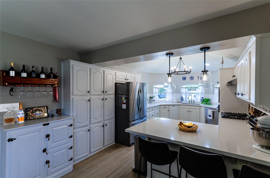 White cabinetry, wood-finish flooring, stainless steel appliances, white subway tile backsplash, and light-toned countertops