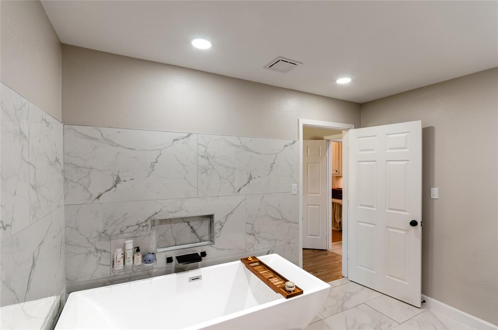 Freestanding soaking tub with a wall-mounted faucet, marble-look tile flooring, and matching marble-look wall tile with an integrated niche