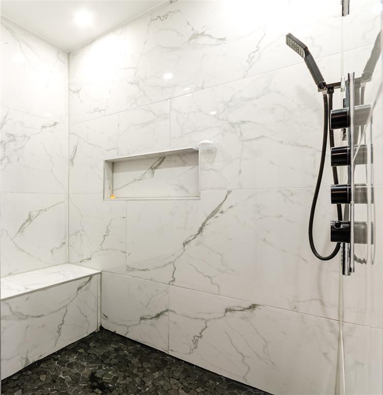Shower with marbled wall tile, built-in bench, recessed niche, and dark pebble floor tile