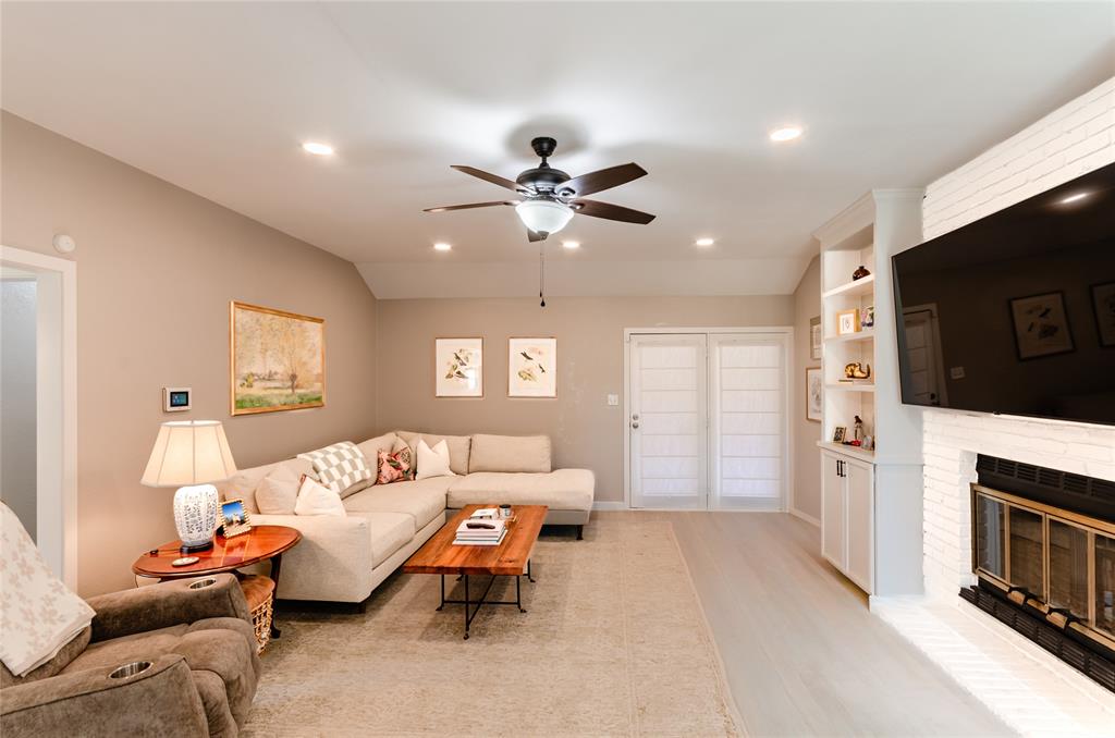 Living area featuring a ceiling fan with light, recessed lighting, a fireplace with a white brick surround, built-in shelving, and wood-finish flooring