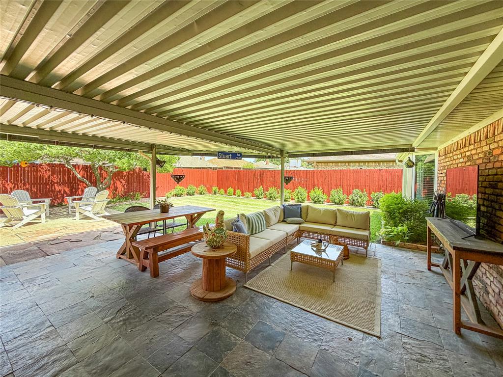 Expansive covered patio with slate-look flooring, exposed brick wall, and a manicured lawn