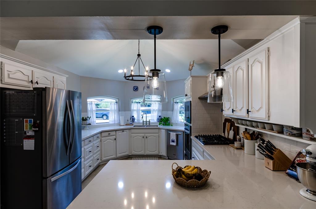 Kitchen featuring white cabinetry, light countertops, a stainless steel refrigerator, a gas cooktop, and pendant lighting