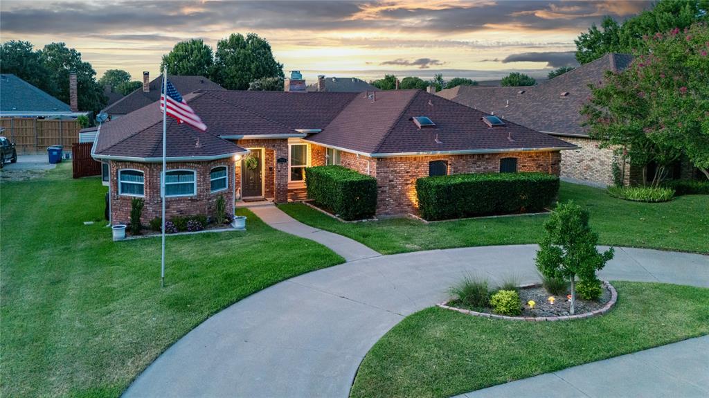 Brick exterior with a brown shingle roof, well-maintained lawn, skylights, and a curved driveway