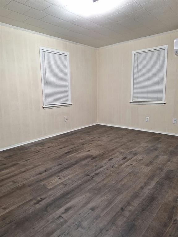 Room interior featuring wood-finish flooring, neutral wall paneling, dual windows with fitted blinds, and a tiled drop ceiling