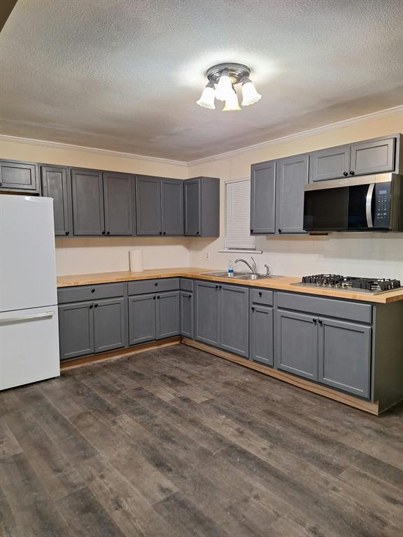Kitchen featuring grey shaker-style cabinetry, wood-finish countertops, stainless steel gas cooktop, built-in microwave, and wood-finish flooring