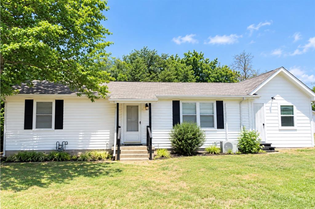 White vinyl siding exterior featuring contrasting black shutters, a shingled gable roof, and concrete steps with black metal railings