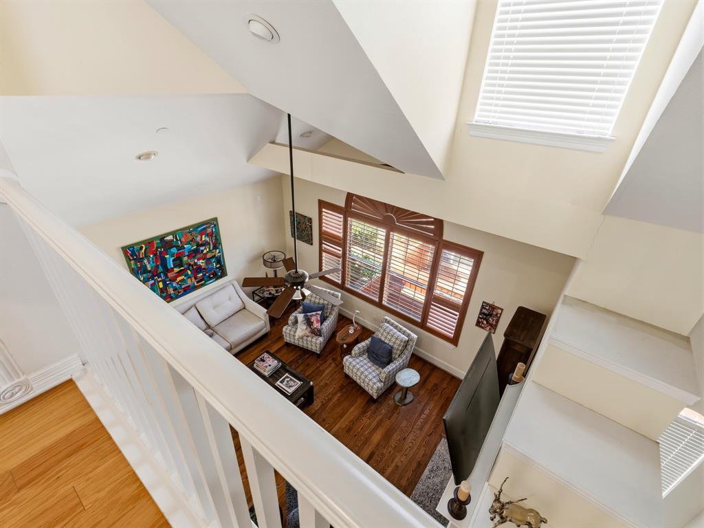 Vaulted ceiling with overhead fan, expansive multi-pane windows with integrated shutters, wood-finish flooring, and white spindle staircase railing