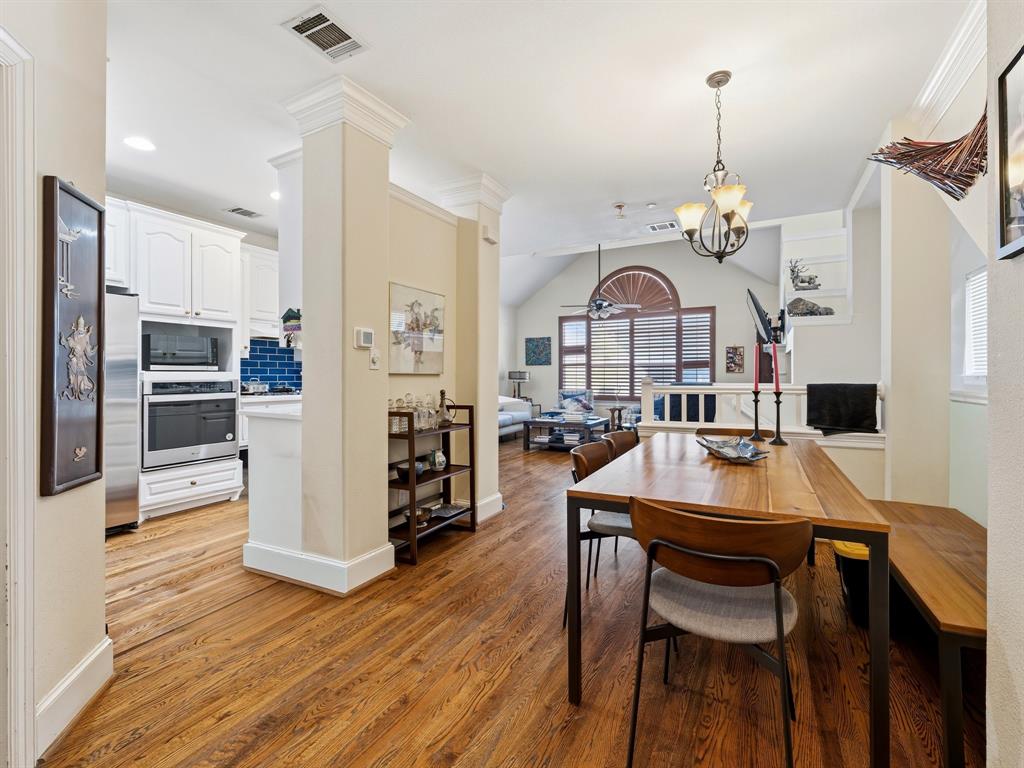 Wood-finish flooring, white cabinetry, built-in stainless steel double oven, arched window with decorative molding, and crown molding