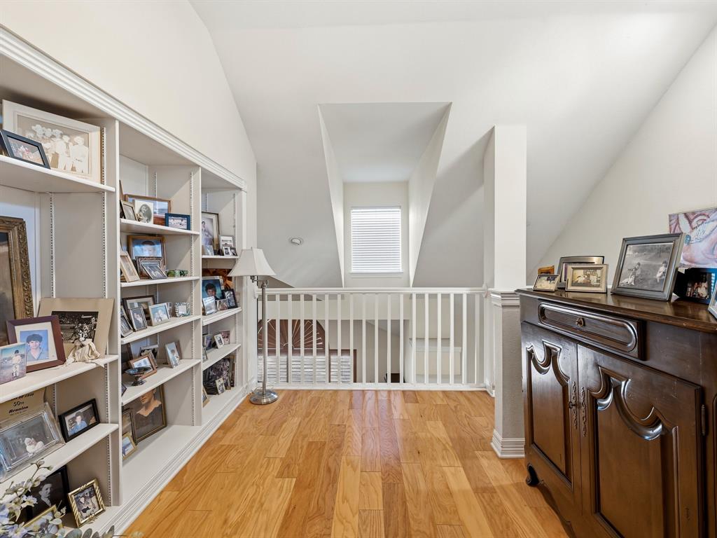 Vaulted ceiling featuring built-in floor-to-ceiling shelving, wood-finish flooring, and a white balustrade railing