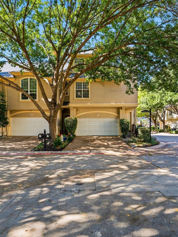 Multi-level townhouse exterior featuring stucco siding, arched garage entries, divided-light windows, and a mature tree canopy Multi-level townhouse exterior featuring stucco siding, arched garage entries, divided-light windows, and a mature tree canopy