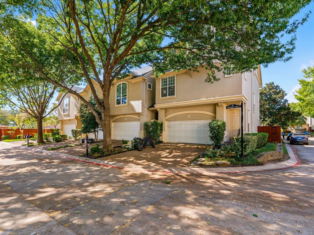 Multi-story exterior featuring a neutral stucco facade, arched windows, attached multi-car garages, and mature shade trees Multi-story exterior featuring a neutral stucco facade, arched windows, attached multi-car garages, and mature shade trees