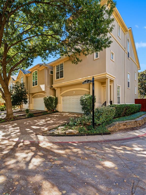 Multi-story exterior featuring a neutral stucco facade, arched garage entries, a textured aggregate driveway, and tiered stone retaining walls Multi-story exterior featuring a neutral stucco facade, arched garage entries, a textured aggregate driveway, and tiered stone retaining walls