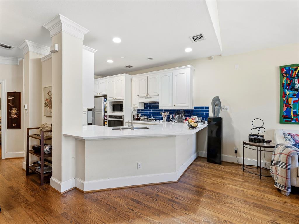 Kitchen featuring white cabinetry, solid-surface countertops, blue subway tile backsplash, built-in stainless steel appliances, and wood-finish flooring