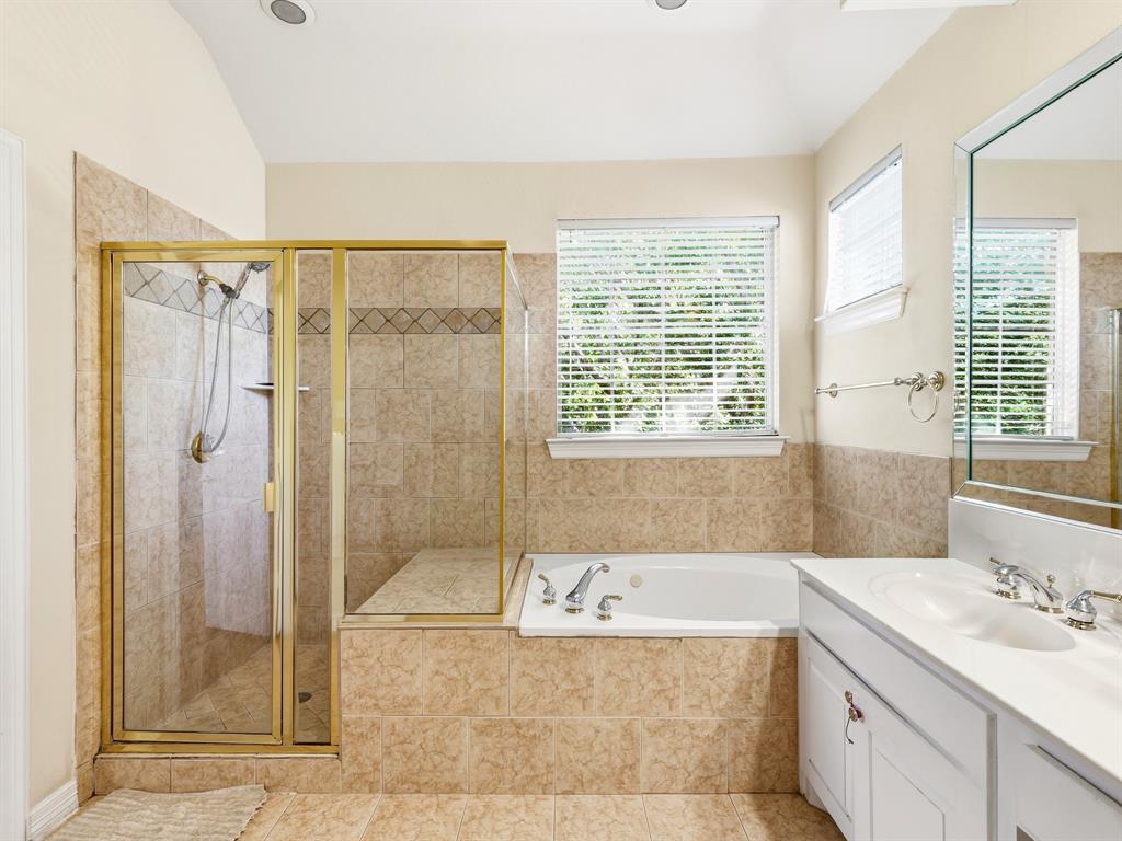 Bathroom featuring a jetted tub, a glass-enclosed shower with tiled surround, white cabinetry, a dual-basin countertop, and a large wall-mounted mirror