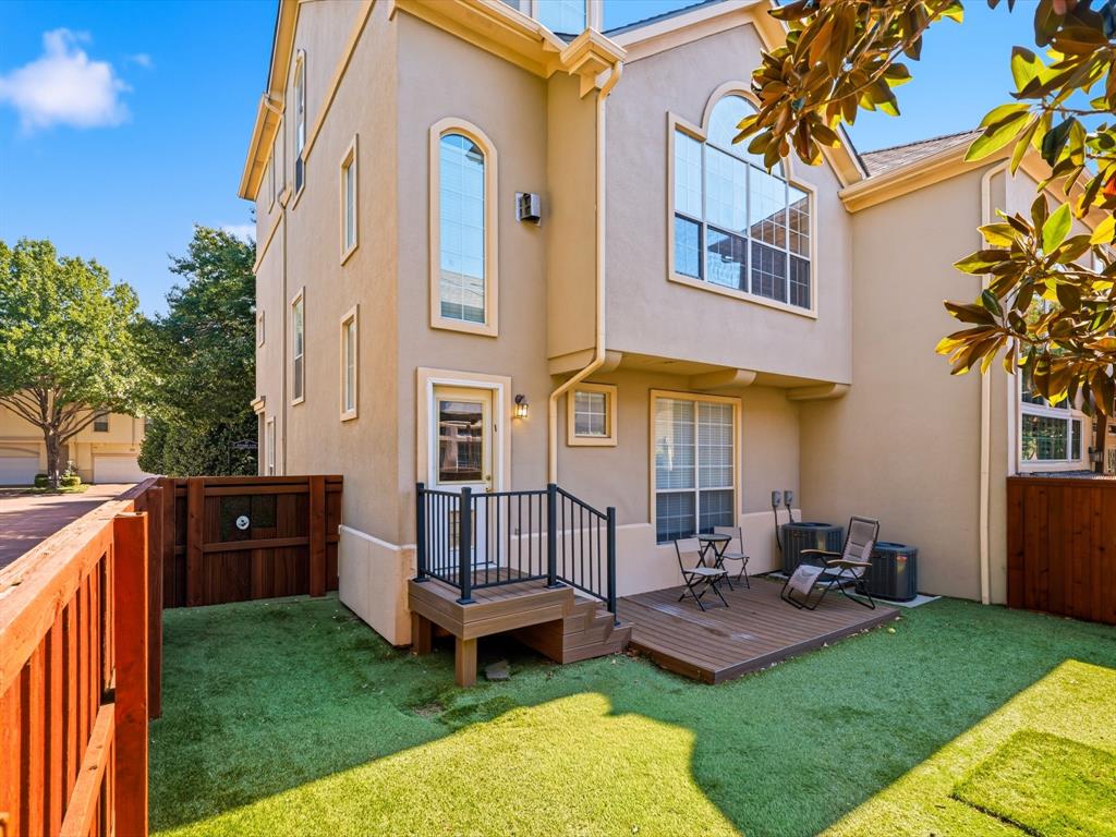 Stucco exterior featuring multi-pane arched windows, raised composite deck with black metal railing, and enclosed yard with perimeter wood fencing