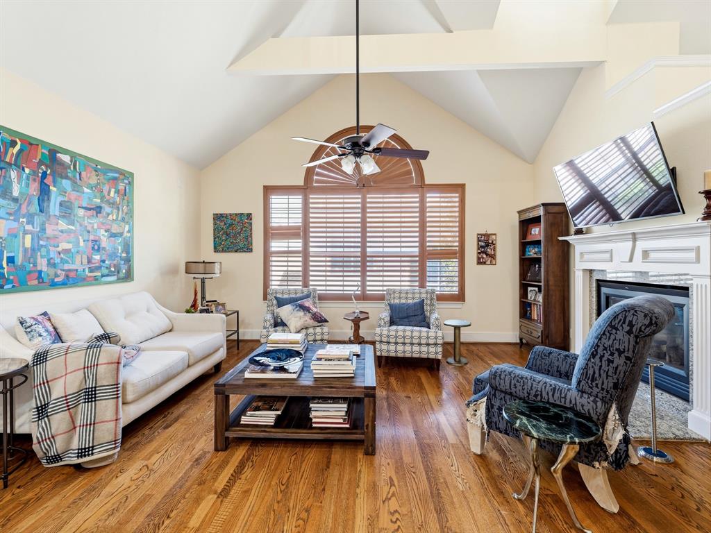 Vaulted ceilings with wood-finish flooring, central ceiling fan, arched window, and a built-in fireplace featuring a decorative mantel