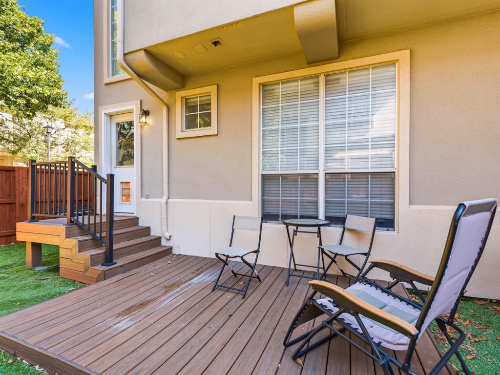 Rear exterior featuring a multi-level wood-finish deck, metal railing, exterior wall-mounted light fixture, and a glass-panel door
