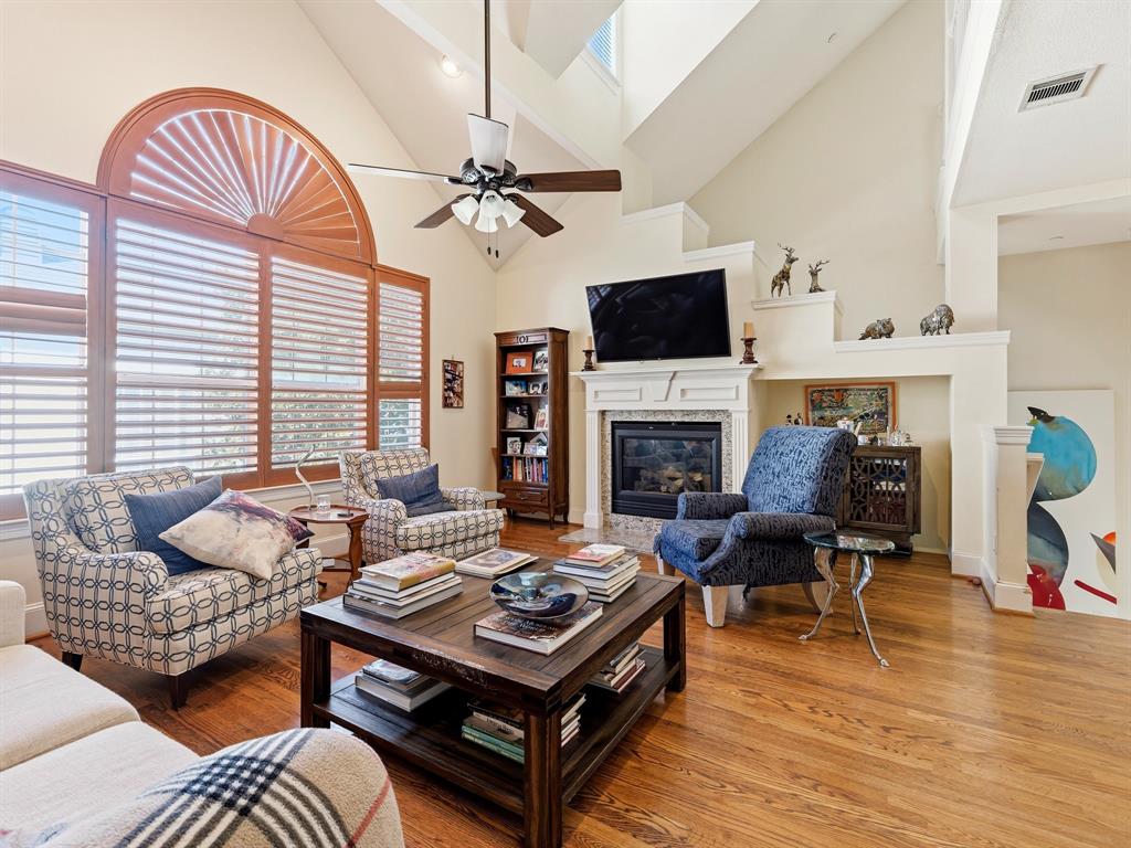 Vaulted ceilings featuring a large arched window with plantation shutters, wood-finish flooring, and a fireplace with a decorative mantle and tile surround Vaulted ceilings featuring a large arched window with plantation shutters, wood-finish flooring, and a fireplace with a decorative mantle and tile surround