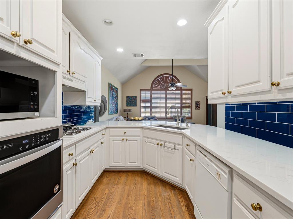 Kitchen featuring white cabinetry, solid-surface countertops, blue subway tile backsplash, built-in stainless steel oven and microwave, and wood-finish flooring Kitchen featuring white cabinetry, solid-surface countertops, blue subway tile backsplash, built-in stainless steel oven and microwave, and wood-finish flooring