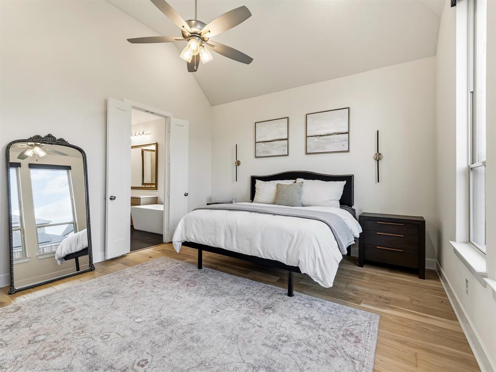 Vaulted ceiling featuring a central brushed-nickel ceiling fan, wood-finish flooring, and wall-mounted light fixtures