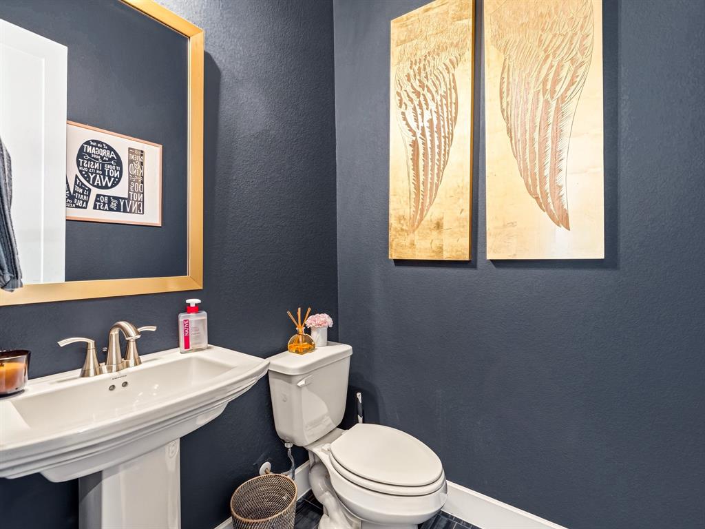 Pedestal sink with polished metal faucet hardware, large-scale gold-toned wall mirror, and dark-toned wall finish