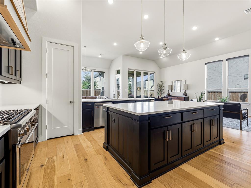 Kitchen featuring a center island with quartz countertop, dark cabinetry, wood-finish flooring, stainless steel built-in range, and glass pendant lighting