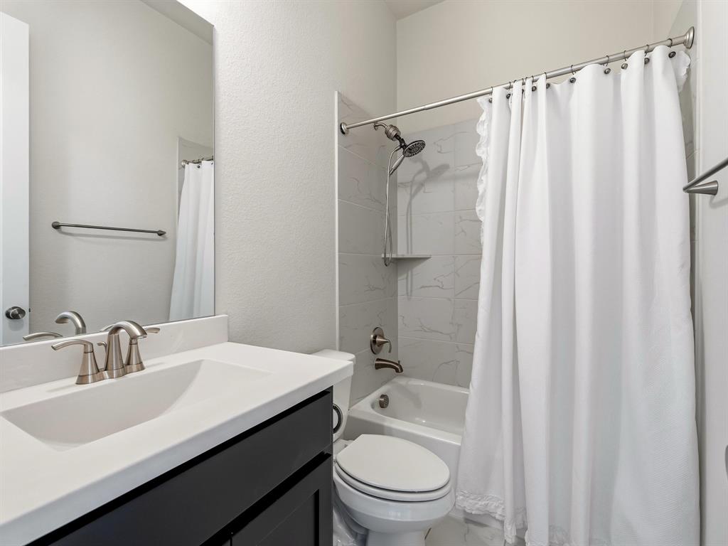 Bathroom featuring a white vanity with a solid surface countertop, an undermount sink with a brushed nickel faucet, a large wall-mounted mirror, and a tub with a tile surround