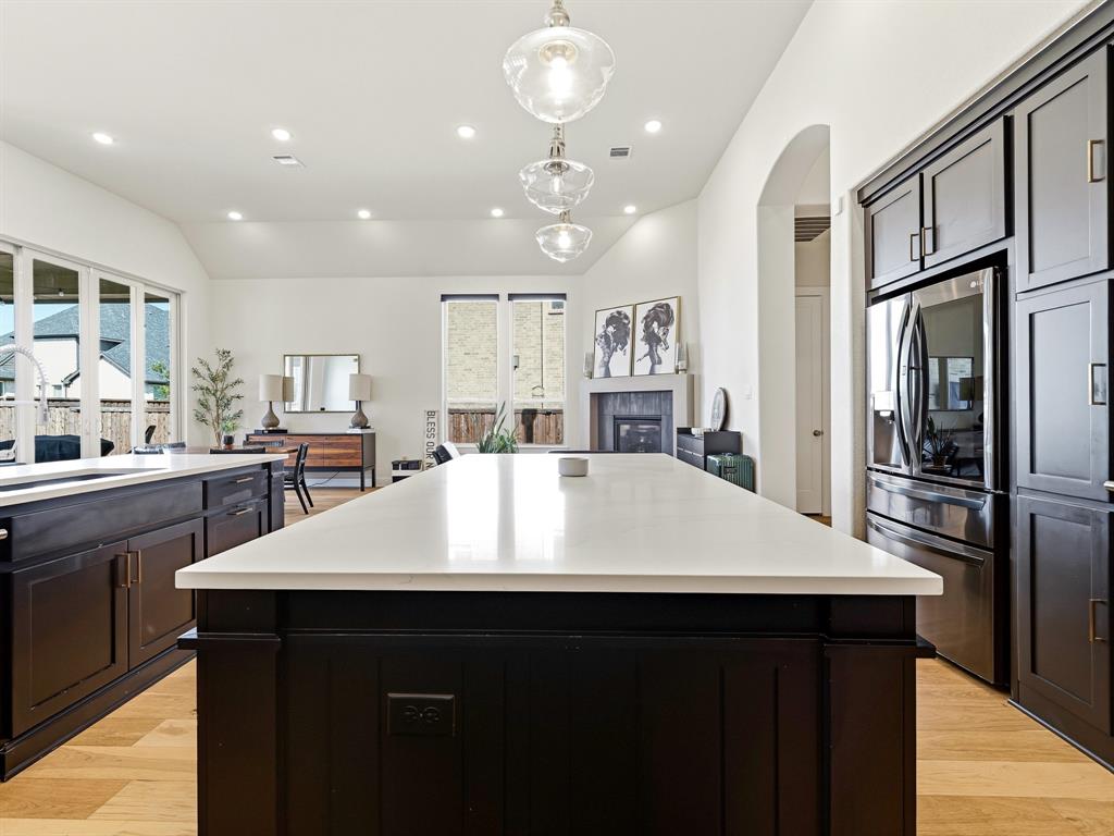 Kitchen featuring an expansive center island with a stone countertop, dark custom cabinetry, recessed lighting, glass pendant fixtures, and wood-finish flooring
