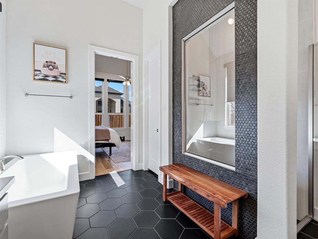 Freestanding soaking tub with a chrome faucet, large-format matte black hexagonal floor tile, and a floor-to-ceiling penny-round tile accent wall featuring a glass panel