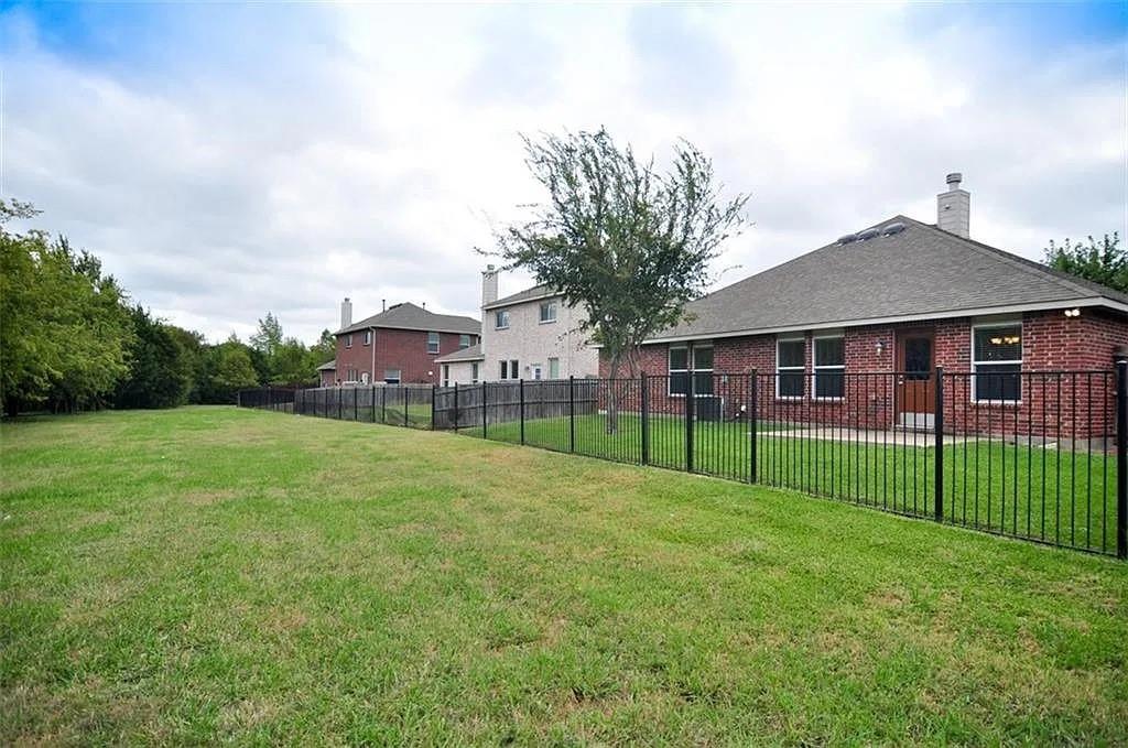 Spacious backyard featuring a brick exterior, shingle roof, and a black metal perimeter fence