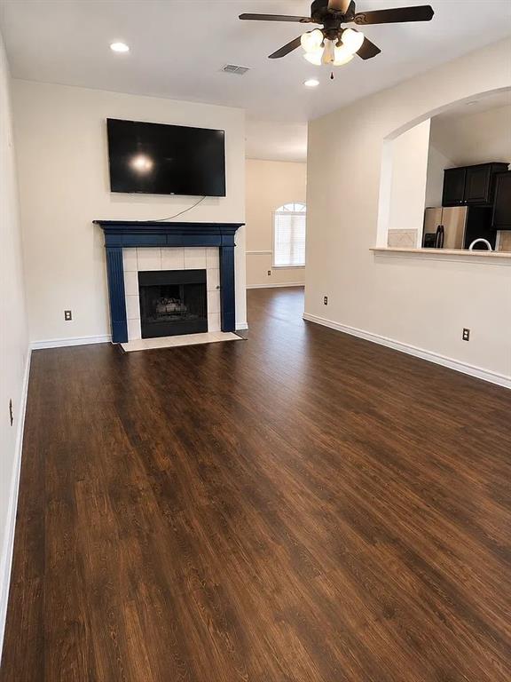 Living area featuring dark wood-finish flooring, recessed lighting, and a fireplace with a mantel and tiled surround Living area featuring dark wood-finish flooring, recessed lighting, and a fireplace with a mantel and tiled surround