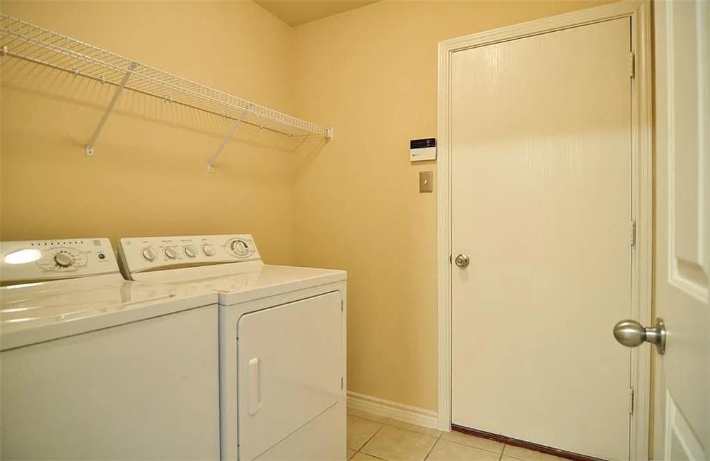 Dedicated laundry space featuring tile flooring, a white interior door with metallic hardware, and white wire shelving