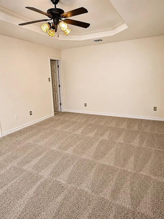 Interior space featuring a recessed tray ceiling, wall-to-wall carpeting, and a central ceiling fan with integrated multi-light fixture
